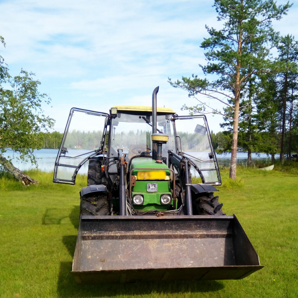 Säkerhetsglas för arbetsfordon traktor, som står på grönt gräs med öppna dörrar